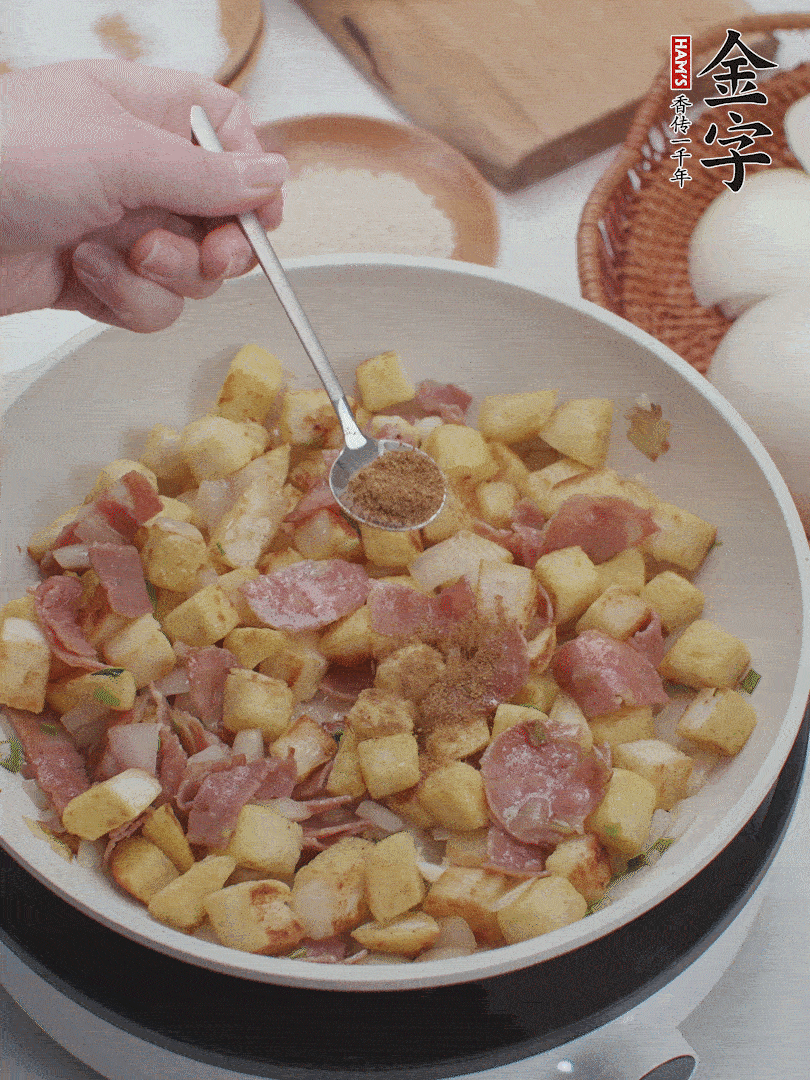起鍋少油，煸香洋蔥丁、蔥白，加入金字培根火腿翻炒幾下，再加入饅頭丁、1小勺孜然粉、少許鹽翻炒均勻并鋪平。